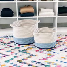 two baskets sitting on top of a rug in front of white shelves filled with folded clothes