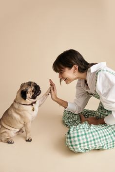 a woman kneeling on the ground petting a pug dog with its paw in it's mouth