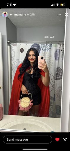 a woman taking a selfie in a bathroom mirror holding a cupcake and wearing a red cape