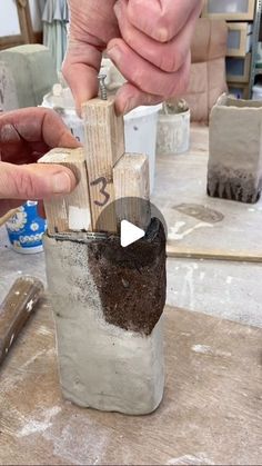 two hands are working on some kind of object that is made out of cement and wood