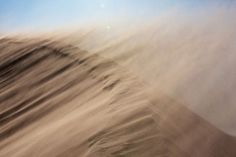 sand blowing in the wind on a sunny day with blue sky and sun behind it