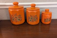 three orange canisters sitting on top of a wooden table next to a wall