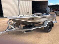 a silver boat is parked in front of a metal building with two tires on the trailer