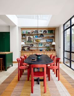 the dining room table is surrounded by red chairs and green cabinetry with open shelves