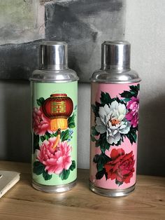 two tins with flowers painted on them sitting on a table