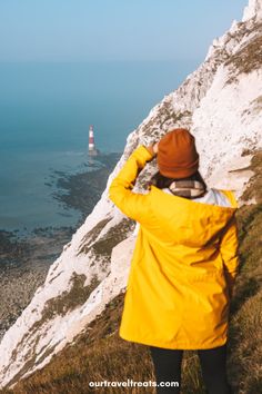 a person standing on top of a hill looking at the ocean with a lighthouse in the distance