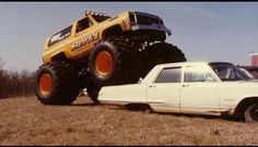 a large monster truck on top of a white car in a field next to other cars