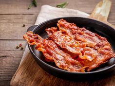 cooked bacon in a skillet on a wooden cutting board