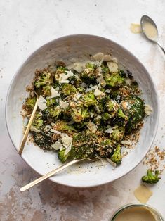 a white bowl filled with broccoli and cheese next to a cup of sauce