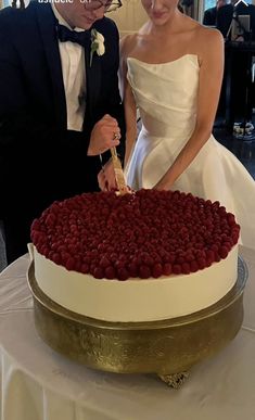 a man and woman cutting into a large cake on top of a white table cloth