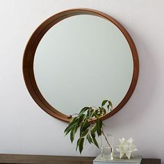 a round mirror hanging on the wall above a table with a vase and plant in it