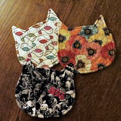 three baby bibs with flowers on them sitting on a wooden table next to each other