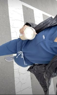 a man in blue shirt and black pants holding a white cup over his head while standing on the street