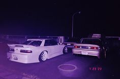 two cars parked next to each other in a parking lot at night with purple light