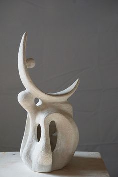 a white sculpture sitting on top of a table next to a gray wall in the background