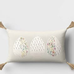 three embroidered eggs on a white pillow with tassels and flowers in the middle