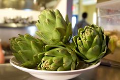 a white bowl filled with green artichokes on top of a counter