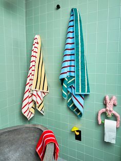 two towels hanging on the wall in a bathroom with green tiled walls and blue tiles