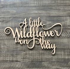 a wooden sign that says, little wildflower on the way in cursive writing