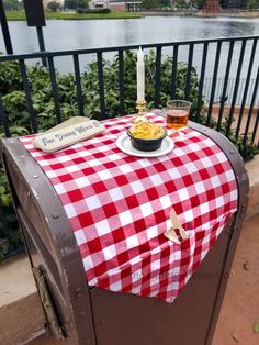 a red and white checkered table cloth on top of a trash can with a plate of food next to it