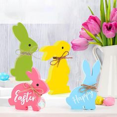 three wooden easter bunnies sitting on top of a table next to pink tulips