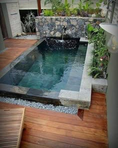 an outdoor swimming pool in the middle of a wooden decked area with plants and rocks