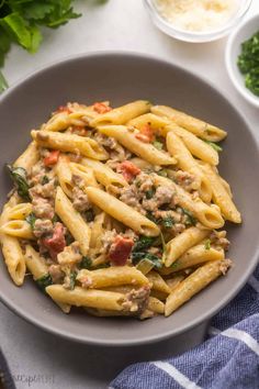 pasta with sausage and spinach in a grey bowl on a blue towel next to bowls of parsley