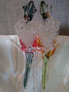 two glass vases with flowers in them sitting on a white cloth covered tablecloth