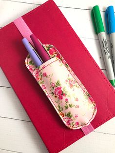 three pens and two markers in a pink holder