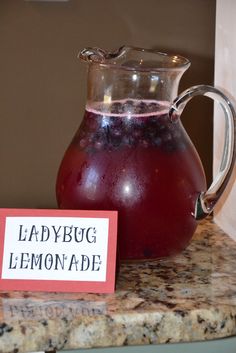 a glass pitcher filled with liquid sitting on top of a counter next to a sign that says ladybug lemonade