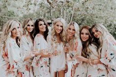 a group of women standing next to each other wearing robes and holding champagne flutes in their hands