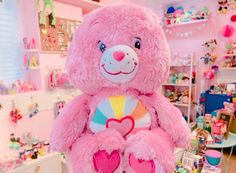 a large pink teddy bear sitting on top of a wooden floor in a room filled with toys