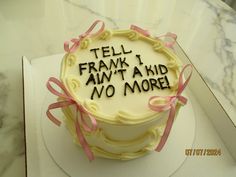 a cake with writing on it sitting on top of a white table next to a pink ribbon