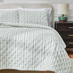 a bed with white and green striped comforter on top of it next to a night stand