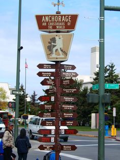 a pole with many signs on it in the middle of a city street and people walking by