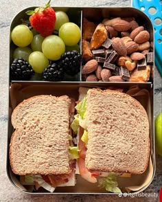 a lunch box filled with fruit, nuts and sandwich on top of a countertop