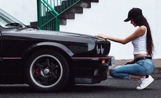 a woman kneeling down next to a black car