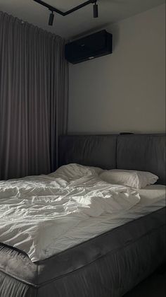 an unmade bed sitting in front of a window with curtains on the windowsill