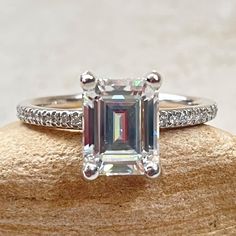 an emerald cut diamond ring sitting on top of a rock