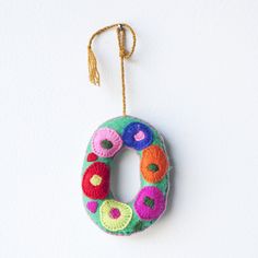 a felt ornament hanging from a string on a white wall, decorated with multicolored flowers