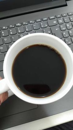 a person is holding a cup of coffee in front of a laptop computer with the keyboard on it