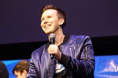 a man holding a microphone in his right hand and wearing a leather jacket on stage