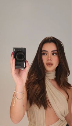 a woman holding up a camera in front of her face and wearing a tan dress