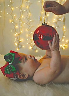 a baby laying on its back with a christmas ornament hanging from it's head