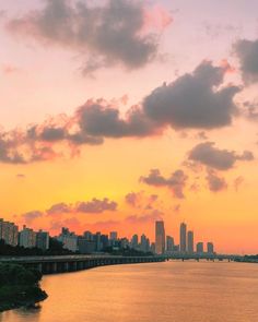 the sun is setting over the city and water in front of it, as seen from across the river