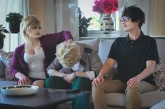 three people sitting on a couch in front of a table with a bowl of food