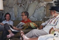 three older people sitting on a couch reading newspapers