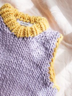 a purple and yellow knitted sweater laying on top of a white sheet with a tag