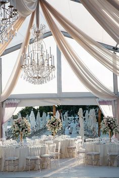 a room filled with lots of tables covered in white cloths and chandeliers