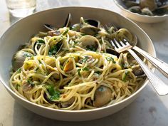 a white bowl filled with pasta and clams on top of a table next to silverware